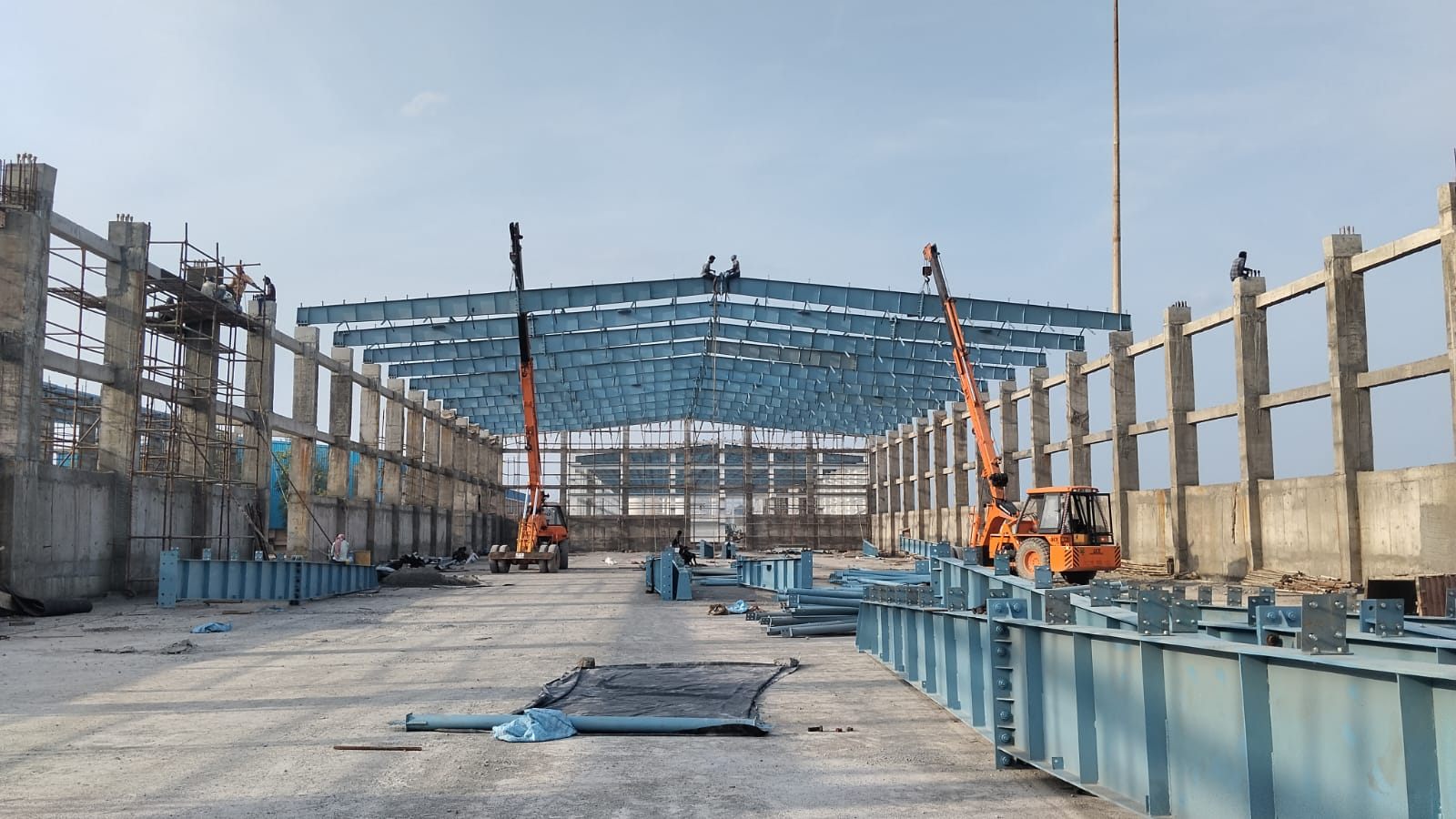 A long shed taking its roof, two cranes working the rafters down the line