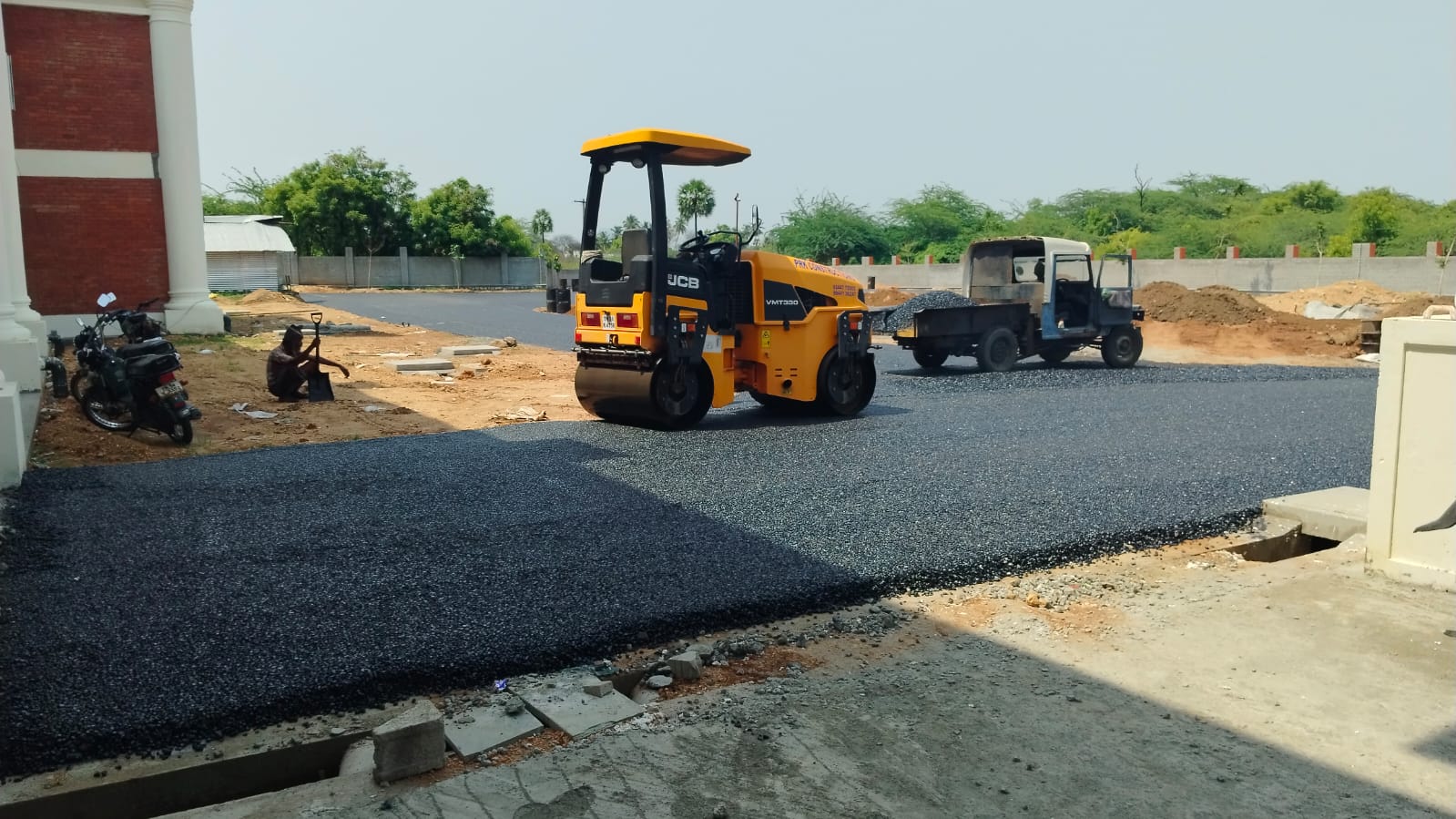 Tandem roller compacting a fresh bituminous surface up to the kerb line and the new drain